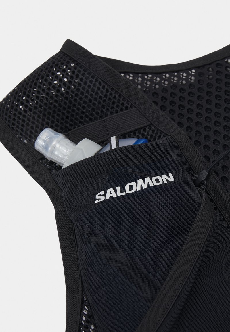 Gilet de hydration en mesh noir avec une bouteille d'eau grise maintenue dans une poche, avec le logo "SALOMON" affiché en évidence. Design durable et léger.