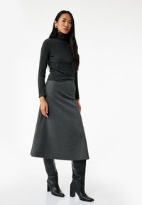 Grå rullekraveshirt parret med en grå ribbet maxi-nederdel, suppleret med knæhøje sorte hæle støvler. Glat tekstur hele vejen igennem.