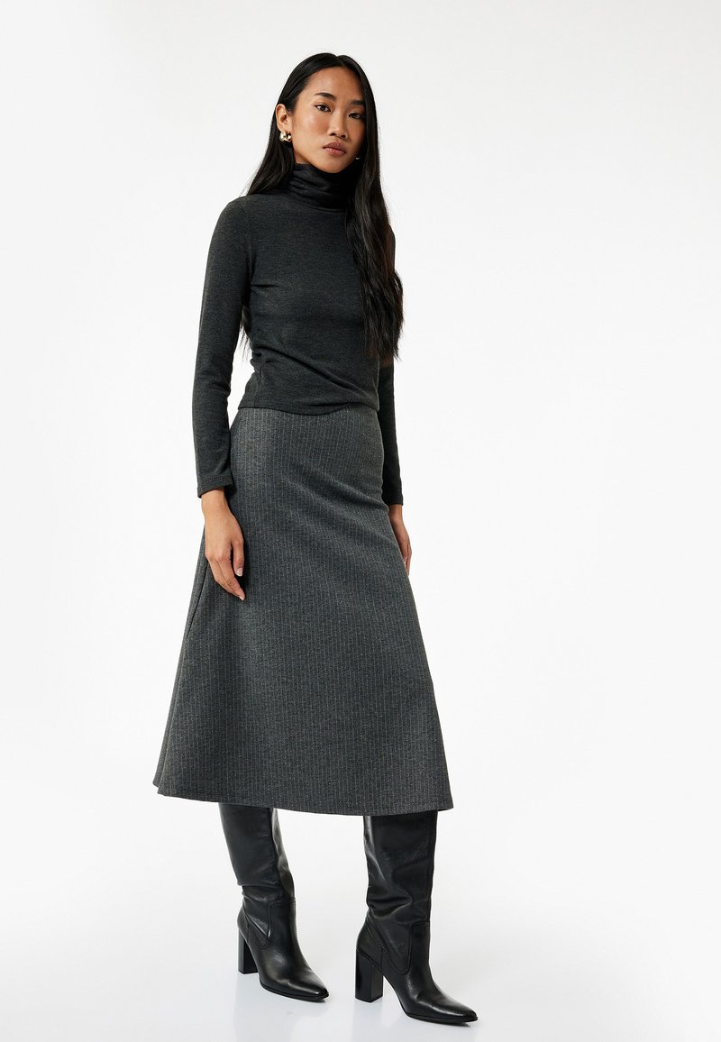 Top de cuello alto gris combinado con una falda larga de canalé gris, complementado con botas de tacón altas negras. Textura suave en todo.