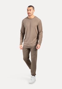 Langärmliges, hellbraunes Hemd, kombiniert mit passenden braunen Hosen, die ein einfaches Design und eine glatte Textur aufweisen, getragen mit weißen Turnschuhen.