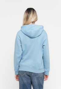 Light blue hoodie with a spacious hood, ribbed cuffs and hem, made of soft fabric. Worn with blue jeans, showcasing a casual style.