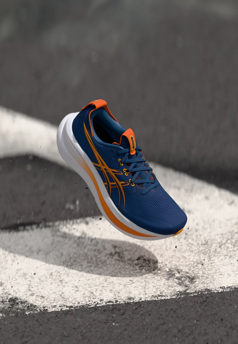 Scarpa da corsa di colore blu scuro con dettagli arancioni, tomaia in mesh, suola bianca spessa e design dinamico. Presenta il logo e dettagli di cucitura a contrasto.