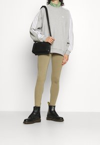 Grå oversized sweatshirt med vita ränder, grön dragkedja vid kragen, beige leggings och svarta kängor. Svart texturerad crossbody-väska som hålls i handen.