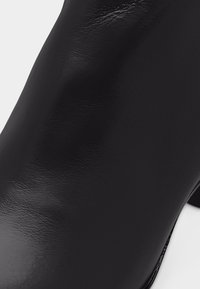 Κοντινή λήψη λείας επιφάνειας μαύρου δέρματος ενός παπουτσιού με ψηλό τακούνι, που αναδεικνύει την υφή και το φινίρισμά του.