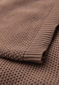 Hnědá pletená látka s texturovaným vzorem včelí plástve, s žebrovanými akcenty podél okraje. Měkký a mírně pružný materiál.