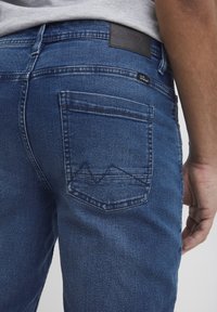 Jeans din denim albastru închis, cu croială dreaptă, un singur buzunar la spate cu un design triangular și o etichetă din piele la talie.