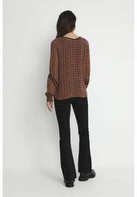 Blusa marrone a fantasia con maniche lunghe e accenti neri, abbinata a pantaloni neri a zampa d'elefante e stivali neri chunky.