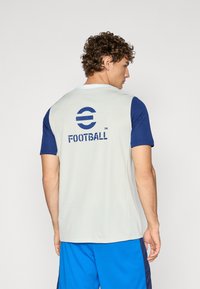 Light gray sports jersey with blue short sleeves, featuring the text "FOOTBALL" and a logo on the back. Made from breathable material.