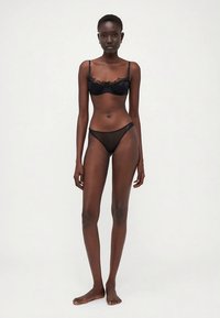 Conjunto de lingerie preta com um soutien tipo bralette com acabamento em renda e cuecas combinando de alças finas. Tecido suave com detalhes transparentes e design delicado.