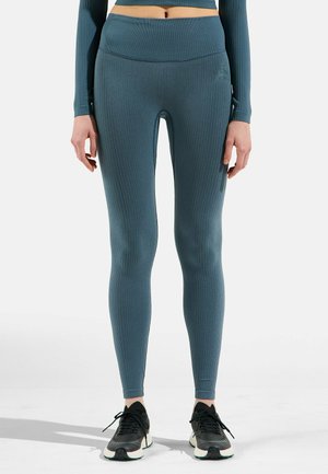 Ribbed, teal leggings made from stretchy fabric; high waistband; subtle branding on side; paired with black athletic shoes.