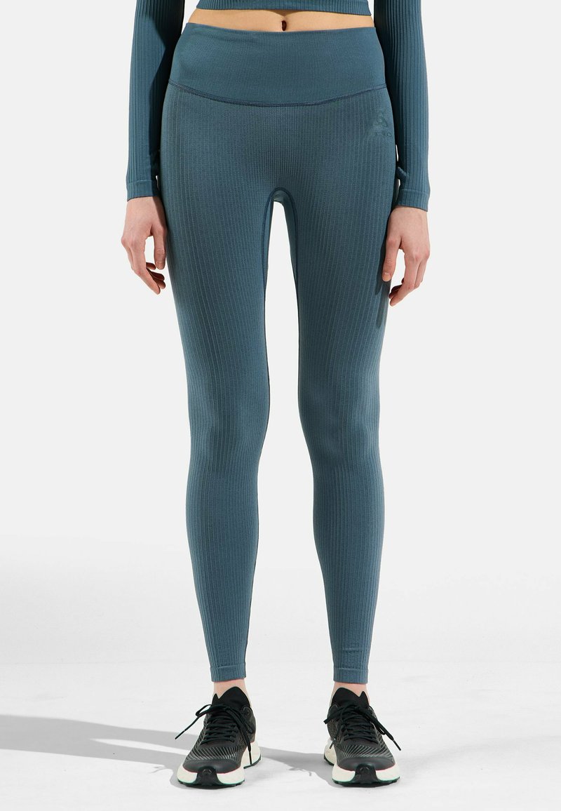 Rippelige, türkisfarbene Leggings aus dehnbarem Stoff; hoher Bund; dezente Markenkennzeichnung an der Seite; kombiniert mit schwarzen Sportschuhen.