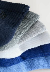 Pile de six chaussettes en maille côtelée dans des tons marine, gris clair, blanc, bleu et bleu clair, disposées en chevauchement sur une surface blanche.