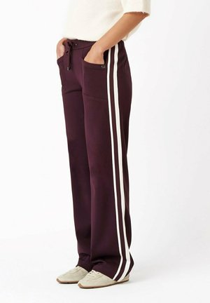 Burgunderfarbene, weit geschnittene Hose mit weißen Seitenstreifen, zwei Fronttaschen und einem verstellbaren Kordelzugbund. Hergestellt aus weichem, dehnbarem Material.