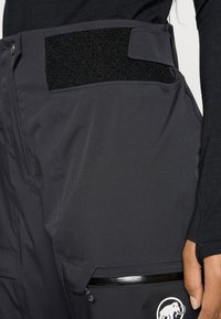 Schwarze Outdoor-Hosen mit einem strukturierten Bund und Klettverschluss. Verfügt über eine Reißverschlusstasche mit einem glänzenden Akzent und einem Logodetail.