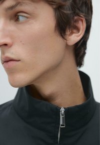 Schwarze Zip-up-Jacke mit hohem Kragen und silbernem Reißverschluss. Glattes Gewebe mit mattem Finish, das ein minimalistisches Design hervorhebt.