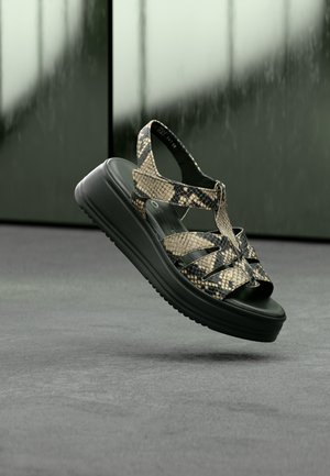 Sleehakken met een bovenwerk van zwart- en beige nepslangenhuid, met riemdetails en een gestructureerde zwarte rubberen zool.