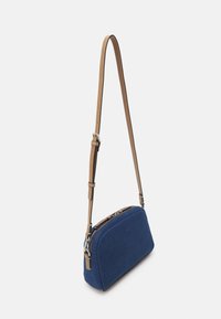 Modrá látková kabelka přes rameno s oblým tvarem, koženým páskem v barvě světle hnědé a stříbrnými detaily na zipu. Hladká textura s minimalistickým designem.