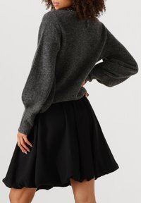 Grijze gebreide trui met ballonmouwen, gecombineerd met een zwarte, uitlopende rok, wat een gelaagd silhouet creëert. Zachte, getextureerde materialen zijn zichtbaar.