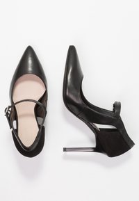 Černé vysoké podpatky se špičatou špičkou, otevřenými stranami a páskem kolem kotníku. Vyrobené z kůže s hladkým, lesklým povrchem a texturovaným podpatkem.