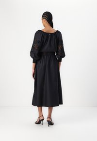 Sort kjole med puffede ærmer og blonder. Skørtet er langt med en samlet talje. Accessoriseret med sorte strophæle.