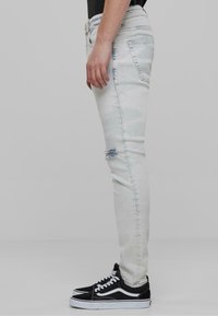 Világoskék, skinny farmernadrág, lyukakkal a térdnél, klasszikus öt zsebes kialakítással. Fekete Vans sportcipővel párosítva.