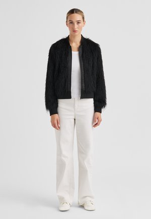 Black faux fur bomber jacket with a zip front, ribbed cuffs, and hem, paired with white wide-leg pants and casual sneakers.