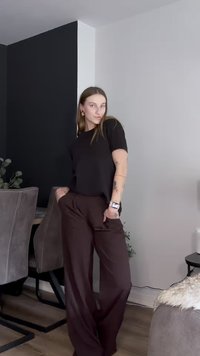 Top nero a maniche corte abbinato a pantaloni ampi marroni. L'outfit ha una vestibilità comoda e il modello è ritratto con le mani nelle tasche.