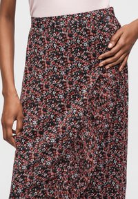 Κοντινό πλάνο χεριών που ρυθμίζουν μια ψηλόμεση φούστα με floral σχέδιο, με κόκκινα, ροζ και λευκά λουλούδια σε μαύρο φόντο.