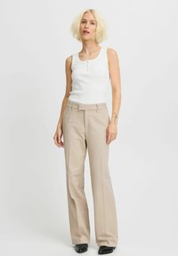 Débardeur blanc à côtes avec trois boutons, associé à un pantalon large beige et des chaussures noires. La tenue présente un design simple et épuré.