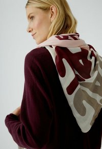 Mehrfarbiger Schal, der über einem dunkelvioletten Pullover drapiert ist, mit einem Muster aus abstrakten Formen in Creme, Burgunderrot und Taupe. Leichter Stoff.