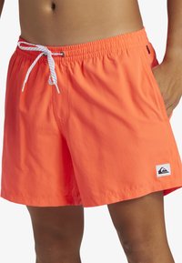 Bañador naranja hecho de tejido ligero, con cinturilla elástica y cordón blanco en contraste, además de bolsillos laterales.