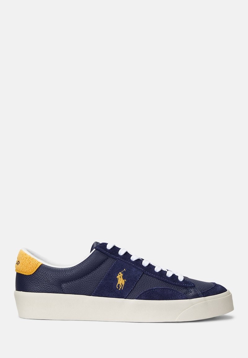 Baskets basses bleu marine avec lacets blancs, semelle blanche, logo jaune sur le côté et patch jaune au talon.