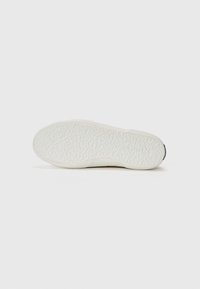 White rubber shoe sole featuring a textured surface with a slightly raised pattern and a contrasting dark accent at the heel.