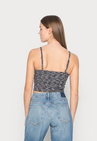 Top cropped com um design texturizado em preto e branco. Apresenta alças finas e é combinado com jeans de cintura alta em azul claro.