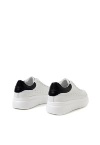 Sneakers bianchi a taglio basso con una tomaia in pelle texturizzata, dettagli in pelle nera sul tallone e una spessa suola in gomma bianca. Design perforato.