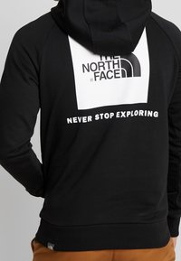 Felpa nera con cappuccio con il logo bianco di "THE NORTH FACE" e la scritta "NEVER STOP EXPLORING" stampata sul retro. Tessuto morbido e polsini a coste.