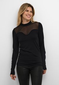 Črna dolga majica z dolgimi rokavi, ki vsebuje prosojno mrežasto območje z valovitim šivom. Blago je gladko, dopolnjeno s prilegajočimi se črnimi hlačami z vzorcem.