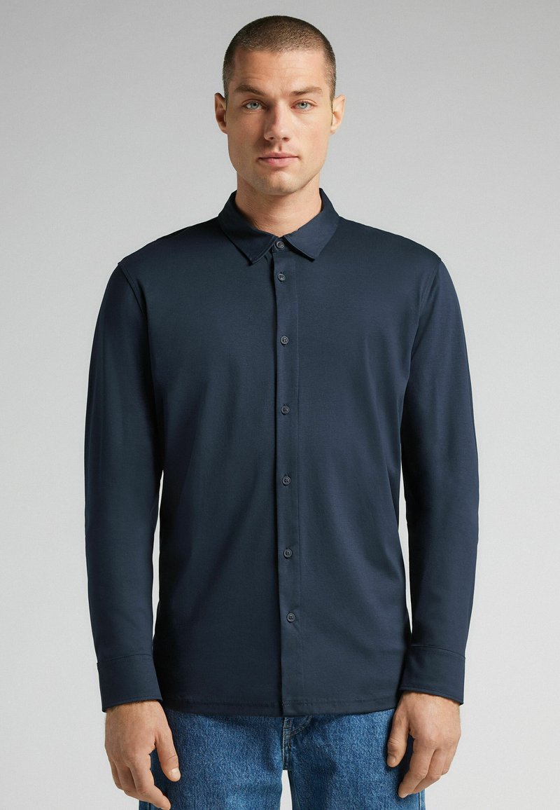 Marineblauwe overhemd met lange mouwen, knoopsluiting, kraag en een gladde textuur; beschikt over bijpassende knopen en een getailleerde pasvorm.