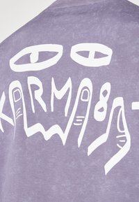Lila Baumwoll-T-Shirt mit einem großen weißen Graf design auf der Rückseite, einschließlich stilisierten Augen und dem Text "KARMA" mit Handzeichen.