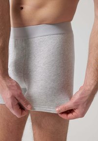 Boxer in cotone grigio con una morbida vita elastica, design aderente e texture liscia, tenuti da mani all'orlo.