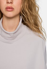 Hellgrauer Rollkragensweater mit weicher, glatter Textur und umgeschlagenem Kragen, der ein tailliertes Design und einen schlichten Rundhalsausschnitt aufweist.