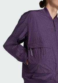 Purple lightweight bomber jacket with a textured finish, zip closure, and side pockets; features a ribbed knit hem and cuffs.