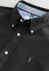 Schwarze Button-Down-Hemd aus Baumwolle. Es hat einen Kragen, weiße Knöpfe, ein hellblau gestreiftes Innenfutter und ein kleines, graues Reh-Logo.
