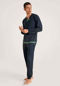 Navyblauw lounge-set gemaakt van zachte stof. De top heeft een henley-kraag met groene accenten, terwijl de broek smalle manchetten heeft.