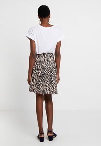 Vit kortärmad t-shirt som kombineras med en mönstrad minikjol i svarta, rosa och beige vågor. Modellen bär marinblå skor med klackar.