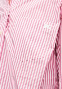 Ροζ και λευκό πουκάμισο με κάθετες ρίγες, που διαθέτει τσέπη στο στήθος με μικρό λογότυπο "MK" κεντημένο σε λευκό χρώμα στην επάνω δεξιά γωνία.