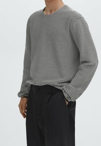 Camicia a maniche lunghe a righe bianche e nere con colletto rotondo, tessuto testurizzato e vestibilità rilassata, abbinata a pantaloni scuri.