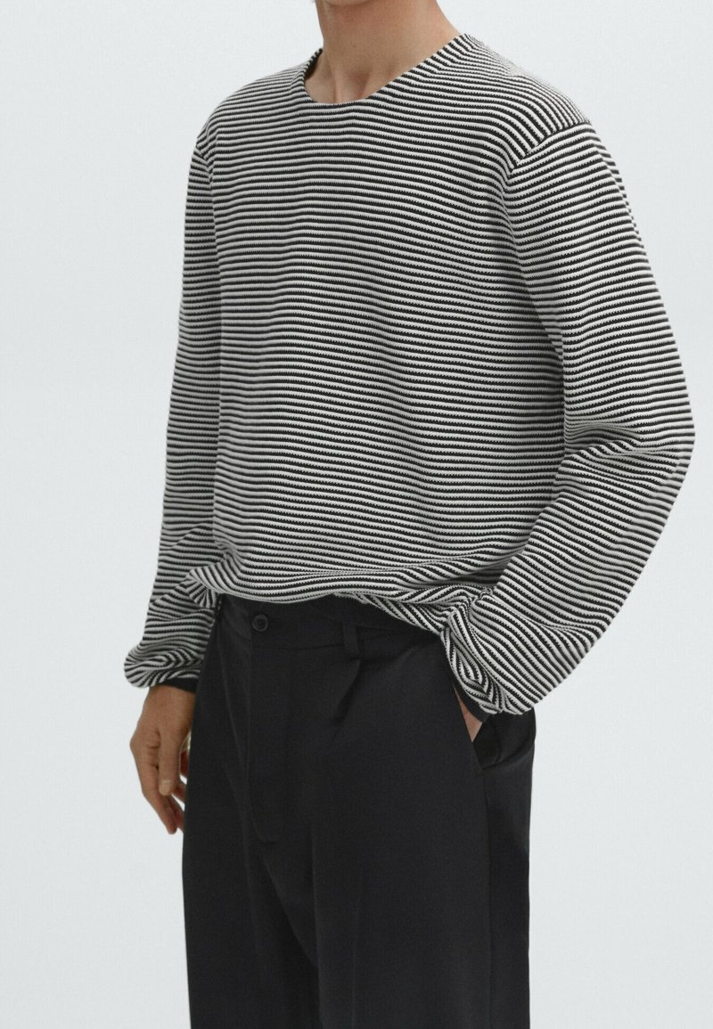 Camicia a maniche lunghe a righe bianche e nere con colletto rotondo, tessuto testurizzato e vestibilità rilassata, abbinata a pantaloni scuri.