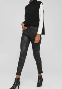 Black sleeveless knit sweater paired with black faux leather pants featuring side zippers and ankle-high heeled boots. Smooth texture overall.