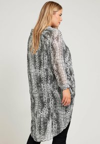 Srebrna i czarna koszula oversized wzorzysta z długimi rękawami i zaokrąglonym dołem; teksturowana tkanina prezentuje wzór w stylu reptilian.